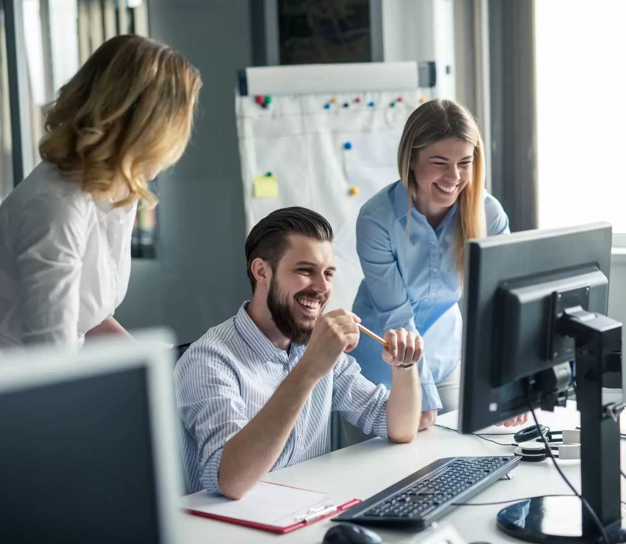 Three Professionals Smiling and Working Together at a Computer.